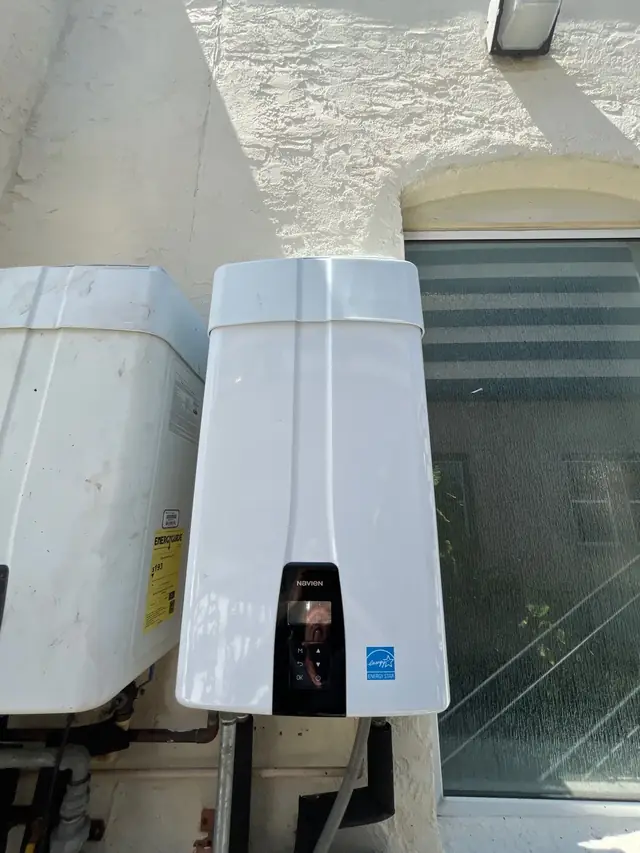 White tankless water heater mounted on an exterior stucco wall beside a tank water heater
