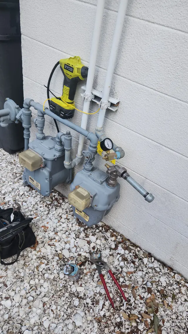 Two residential gas meters with a new gas line and a pressure test gauge fitted on a stucco wall